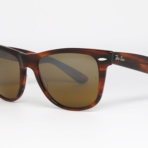 Peut inclure: Lunettes de soleil en &eacute;caille de tortue marron avec des verres bruns et la marque Ray-Ban sur le c&ocirc;t&eacute;.