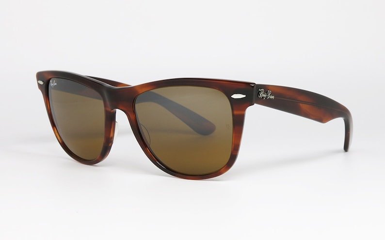 Peut inclure: Lunettes de soleil en &eacute;caille de tortue marron avec des verres bruns et la marque Ray-Ban sur le c&ocirc;t&eacute;.