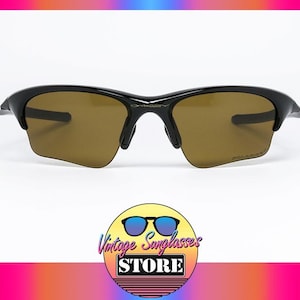 May include: Black sunglasses with brown lenses. The sunglasses have a sleek, modern design with a curved frame. The image includes a logo for a vintage sunglasses store.