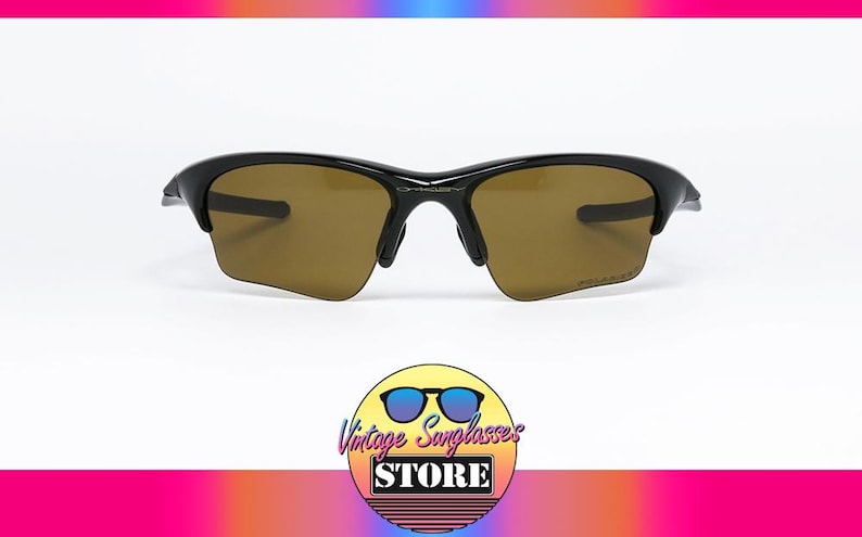 May include: Black sunglasses with brown lenses. The sunglasses have a sleek, modern design with a curved frame. The image includes a logo for a vintage sunglasses store.