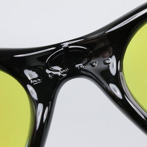 Peut inclure: Gros plan sur des lunettes de soleil noires avec des verres jaunes. Les lunettes de soleil ont une finition brillante et un design incurv&eacute;. Les verres sont de couleur jaune vif et la monture est noire.