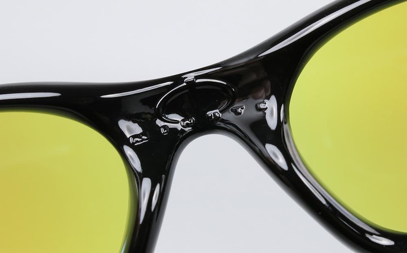 Peut inclure: Gros plan sur des lunettes de soleil noires avec des verres jaunes. Les lunettes de soleil ont une finition brillante et un design incurv&eacute;. Les verres sont de couleur jaune vif et la monture est noire.