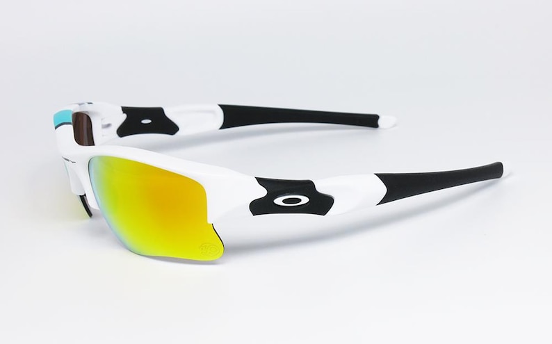 May include: White and black sports sunglasses with a yellow-orange mirrored lens. The sunglasses have a sleek design with black accents and a white frame. The lenses are curved and provide full coverage. The sunglasses are designed for sports and outdoor activities.