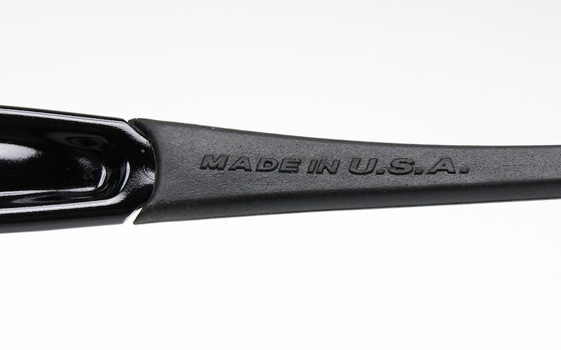 K&ouml;nnte beinhalten: Nahaufnahme eines schwarzen Brillenb&uuml;gels mit dem Text "MADE IN U.S.A." auf dem B&uuml;gel. Der B&uuml;gel besteht aus einem mattschwarzen Material und ist mit einem gl&auml;nzend schwarzen Rahmen verbunden.