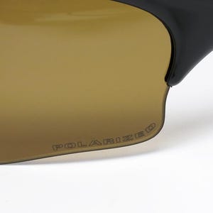 May include: Close-up of sunglasses with brown-tinted lenses and black frames. The word "POLARIZED" is printed on the lens. The sunglasses are designed for outdoor activities and offer protection from the sun.