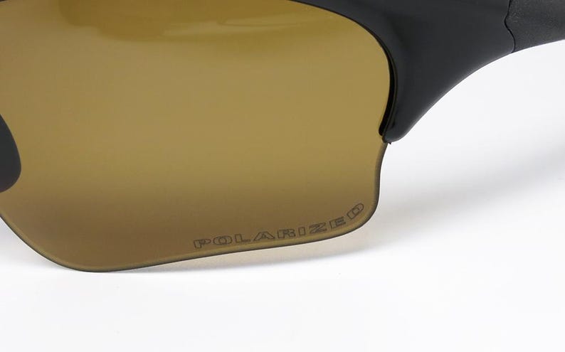 May include: Close-up of sunglasses with brown-tinted lenses and black frames. The word "POLARIZED" is printed on the lens. The sunglasses are designed for outdoor activities and offer protection from the sun.