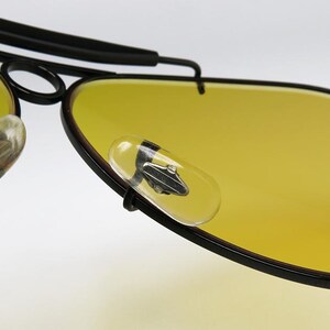 Puede incluir: Primer plano de gafas de sol estilo aviador con lentes amarillas y montura negra. Las lentes son de un amarillo brillante, y la montura es negra y elegante. Incluye almohadillas nasales transparentes. Estas gafas est&aacute;n dise&ntilde;adas para estilo y protecci&oacute;n.