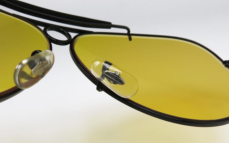 Puede incluir: Primer plano de gafas de sol estilo aviador con lentes amarillas y montura negra. Las lentes son de un amarillo brillante, y la montura es negra y elegante. Incluye almohadillas nasales transparentes. Estas gafas est&aacute;n dise&ntilde;adas para estilo y protecci&oacute;n.