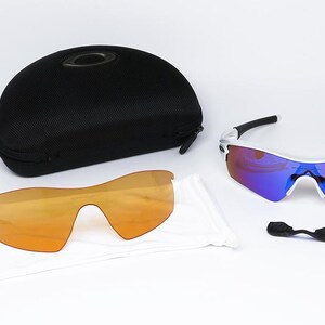 Pu&ograve; includere: Un set di occhiali da sole sportivi con lenti intercambiabili e una custodia nera. Gli occhiali hanno una montatura bianca con dettagli neri e lenti a specchio. Sono incluse lenti aggiuntive color arancione e un nasello.