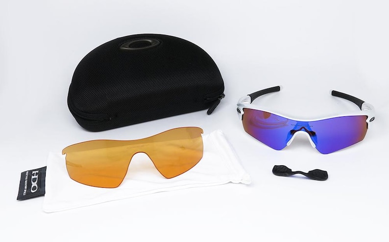 Pu&ograve; includere: Un set di occhiali da sole sportivi con lenti intercambiabili e una custodia nera. Gli occhiali hanno una montatura bianca con dettagli neri e lenti a specchio. Sono incluse lenti aggiuntive color arancione e un nasello.