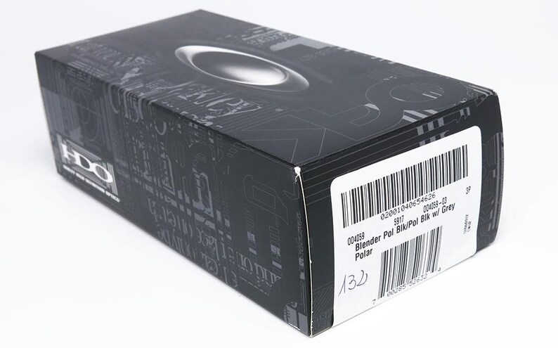 Puede incluir: Una caja rectangular negra con un dise&ntilde;o ovalado plateado en la parte superior. La caja tiene una etiqueta blanca con un c&oacute;digo de barras y el texto "Blender Pol Blk/Pol Blk w/ Grey". La caja tiene un patr&oacute;n gris oscuro.