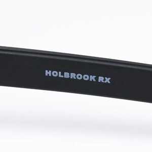 May include: A close-up of a black eyeglass arm with the text "HOLBROOK RX" in white. The arm has a matte black finish and the text is centrally positioned. The material appears to be plastic or a similar substance.