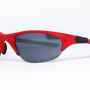 Puede incluir: Gafas de sol rojas con lentes grises oscuras. Las gafas tienen una montura curvada y la palabra "DUCATI" est&aacute; impresa en la lente. Las patillas son negras y rojas.