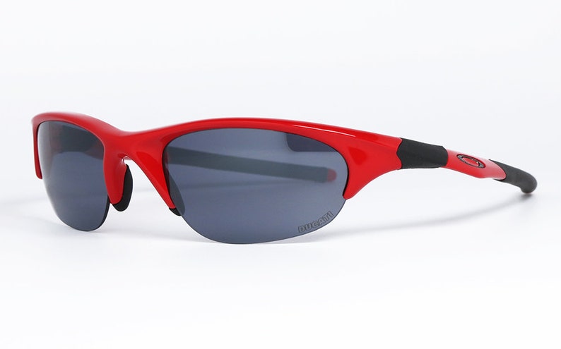 Puede incluir: Gafas de sol rojas con lentes grises oscuras. Las gafas tienen una montura curvada y la palabra "DUCATI" est&aacute; impresa en la lente. Las patillas son negras y rojas.