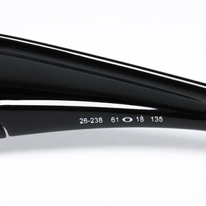 May include: Close-up of a black sunglasses arm with the numbers 26-238, 61, 18, and 135 printed in white. The sunglasses arm is glossy and curved, with a matte black section at the end.
