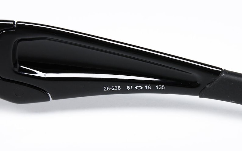 May include: Close-up of a black sunglasses arm with the numbers 26-238, 61, 18, and 135 printed in white. The sunglasses arm is glossy and curved, with a matte black section at the end.