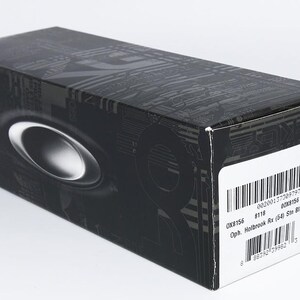May include: Black rectangular box with a silver oval design and a white label with a barcode. The box has a textured pattern and the brand name is visible. The box is for eyewear.