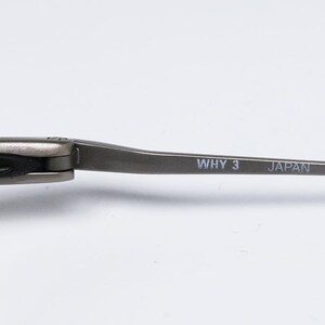 May include: Close-up of the arm of a pair of silver-toned glasses. The arm is marked with the text "WHY 3 JAPAN CE".