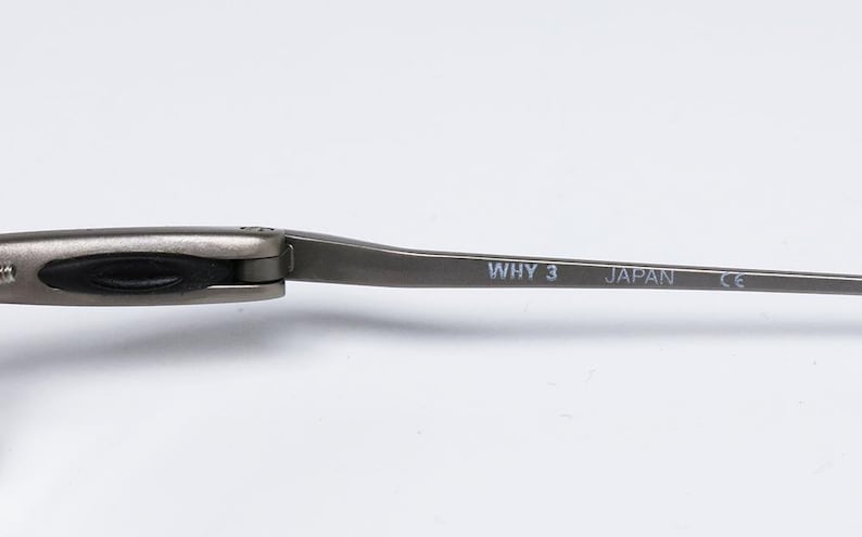 May include: Close-up of the arm of a pair of silver-toned glasses. The arm is marked with the text "WHY 3 JAPAN CE".