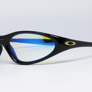 Peut inclure: Lunettes de soleil de sport noires avec une monture incurv&eacute;e et des verres teint&eacute;s bleus. Le logo Oakley est visible sur les branches et la monture. Les verres ont une teinte jaune. Con&ccedil;ues pour le sport et les activit&eacute;s de plein air.