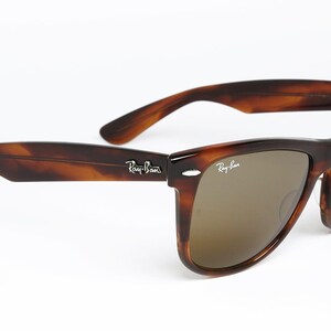 Peut inclure: Lunettes de soleil Ray-Ban en &eacute;caille de tortue brune avec des verres bruns. Les lunettes ont une monture de style Wayfarer classique.