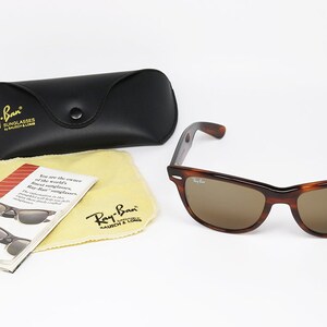 Peut inclure: Lunettes de soleil Ray-Ban en &eacute;caille de tortue marron avec des verres marrons. Les lunettes de soleil sont dans un &eacute;tui noir avec le logo Ray-Ban. L'&eacute;tui est &agrave; c&ocirc;t&eacute; d'un chiffon de nettoyage jaune avec le logo Ray-Ban et une petite brochure avec des informations sur les lunettes de soleil.