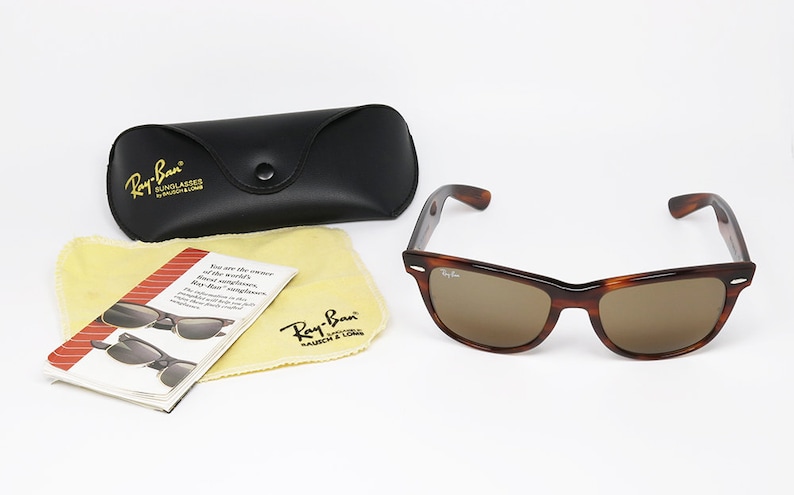 Peut inclure: Lunettes de soleil Ray-Ban en &eacute;caille de tortue marron avec des verres marrons. Les lunettes de soleil sont dans un &eacute;tui noir avec le logo Ray-Ban. L'&eacute;tui est &agrave; c&ocirc;t&eacute; d'un chiffon de nettoyage jaune avec le logo Ray-Ban et une petite brochure avec des informations sur les lunettes de soleil.