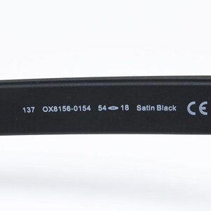 May include: Close-up of a black eyeglass arm with the following text: 137 OX8156-0154 54-18 Satin Black CE. The arm is made of a matte black material.