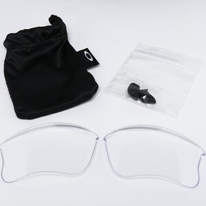 May include: Clear replacement lenses for sunglasses, along with a black drawstring pouch and a small plastic bag containing black nose pads. The lenses are curved and appear to be made of a transparent material.