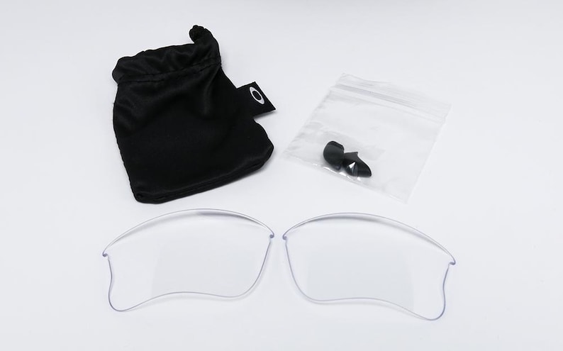 May include: Clear replacement lenses for sunglasses, along with a black drawstring pouch and a small plastic bag containing black nose pads. The lenses are curved and appear to be made of a transparent material.