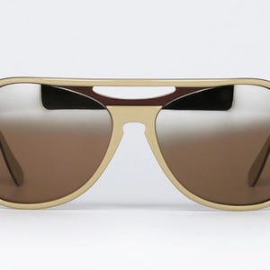 May include: Aviator-style sunglasses with a cream-colored frame and gradient brown lenses. The top bar features a dark burgundy accent. The lenses transition from a light silver at the top to a darker brown at the bottom.