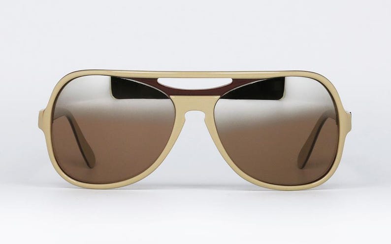 May include: Aviator-style sunglasses with a cream-colored frame and gradient brown lenses. The top bar features a dark burgundy accent. The lenses transition from a light silver at the top to a darker brown at the bottom.