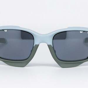 May include: Light blue and gray sunglasses with dark gray lenses. The sunglasses have a unique design with a light blue frame and gray accents. The lenses are a dark gray color, providing protection from the sun.