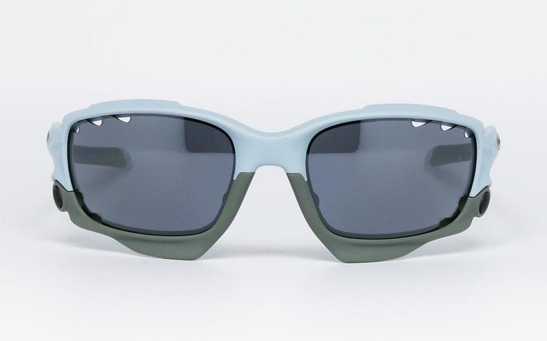 May include: Light blue and gray sunglasses with dark gray lenses. The sunglasses have a unique design with a light blue frame and gray accents. The lenses are a dark gray color, providing protection from the sun.