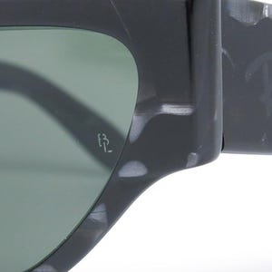 May include: Close-up of a pair of black and white marbled sunglasses with green lenses. The sunglasses have the Ray-Ban logo on the side and the letters "RB" on the inside of the right lens.