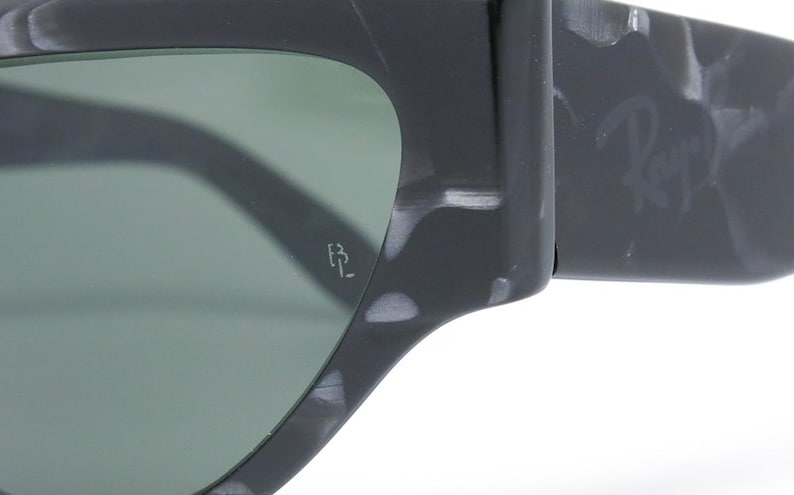 May include: Close-up of a pair of black and white marbled sunglasses with green lenses. The sunglasses have the Ray-Ban logo on the side and the letters "RB" on the inside of the right lens.