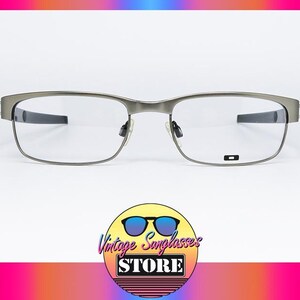 May include: Silver rectangular eyeglasses with clear lenses. The frames have a modern design. The image includes a logo at the bottom and a colourful gradient background.