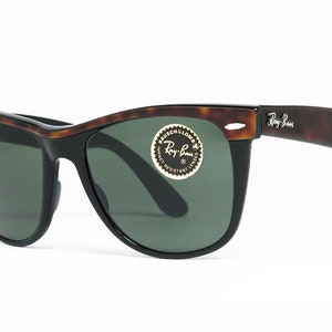 K&ouml;nnte beinhalten: Schildpattfarbene Ray-Ban Sonnenbrille mit gr&uuml;nen Gl&auml;sern. Die Sonnenbrille hat einen schwarzen Rahmen und ein goldenes Ray-Ban Logo am rechten B&uuml;gel.