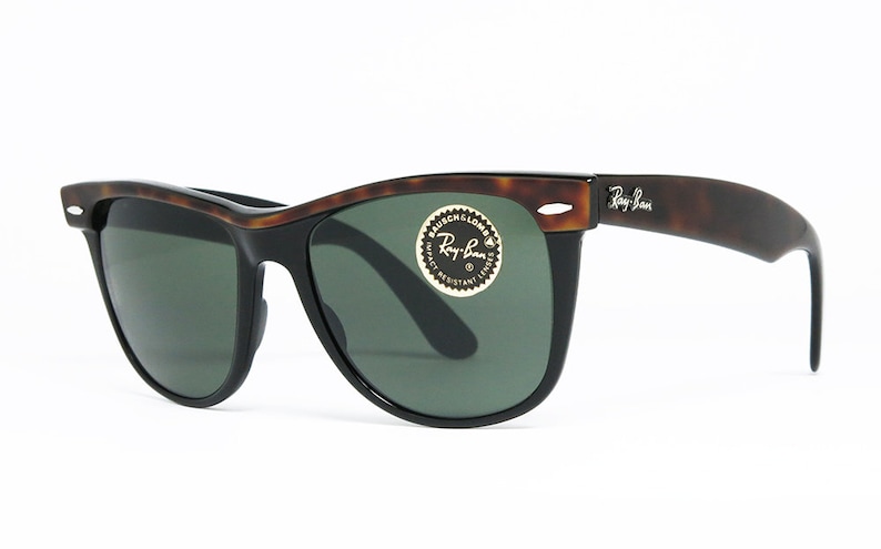 K&ouml;nnte beinhalten: Schildpattfarbene Ray-Ban Sonnenbrille mit gr&uuml;nen Gl&auml;sern. Die Sonnenbrille hat einen schwarzen Rahmen und ein goldenes Ray-Ban Logo am rechten B&uuml;gel.