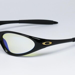 Peut inclure: Lunettes de soleil noires au design &eacute;pur&eacute; et incurv&eacute;. Les verres ont une teinte jaune, et les montures sont noires avec un logo dor&eacute; sur les branches. Les branches ont une prise en caoutchouc. Un accessoire de lunetterie moderne.