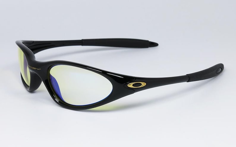 Peut inclure: Lunettes de soleil noires au design &eacute;pur&eacute; et incurv&eacute;. Les verres ont une teinte jaune, et les montures sont noires avec un logo dor&eacute; sur les branches. Les branches ont une prise en caoutchouc. Un accessoire de lunetterie moderne.
