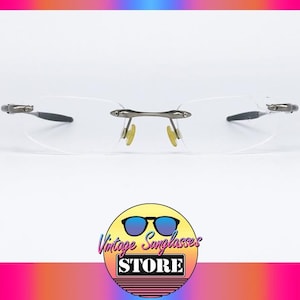 May include: A pair of rimless, silver-toned eyeglasses with clear lenses. The glasses have a simple, modern design.