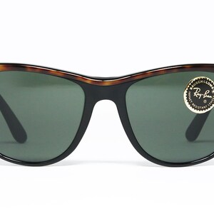 K&ouml;nnte beinhalten: Eine Sonnenbrille von Ray-Ban in Schildpatt-Optik mit gr&uuml;nen Gl&auml;sern. Die Sonnenbrille hat einen schwarzen Rahmen und ein goldenes Ray-Ban-Logo auf der rechten Linse.