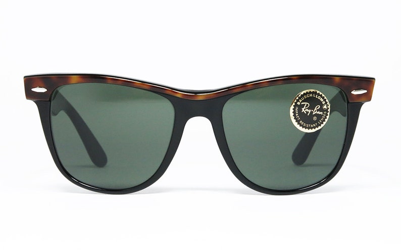 K&ouml;nnte beinhalten: Eine Sonnenbrille von Ray-Ban in Schildpatt-Optik mit gr&uuml;nen Gl&auml;sern. Die Sonnenbrille hat einen schwarzen Rahmen und ein goldenes Ray-Ban-Logo auf der rechten Linse.