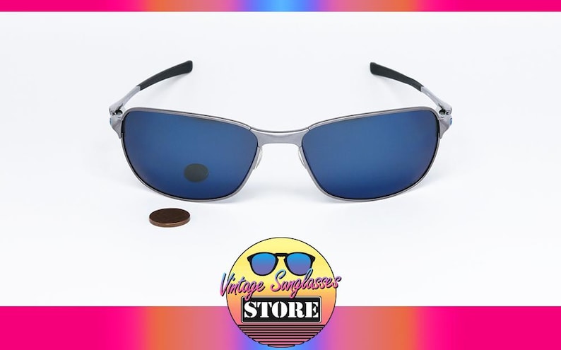 May include: Silver-framed sunglasses with blue lenses. The glasses have a rectangular shape and black arms. A penny is next to the sunglasses. The image also includes a logo that says "Vintage Sunglasses Store".