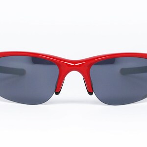 Puede incluir: Gafas de sol rojas con lentes gris oscuro. Las gafas tienen un dise&ntilde;o curvo y deportivo con un acabado brillante. La montura es de color rojo vibrante y las lentes son de color gris oscuro. Las gafas est&aacute;n dise&ntilde;adas para actividades al aire libre.