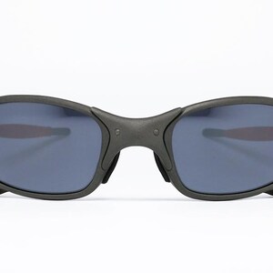 May include: Black sunglasses with a matte finish. The lenses are a dark blue color. The frame has a curved design and a bridge that connects the two lenses. The temples are thin and curve around the ears.
