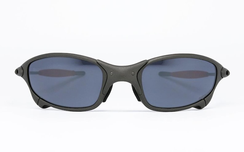 May include: Black sunglasses with a matte finish. The lenses are a dark blue color. The frame has a curved design and a bridge that connects the two lenses. The temples are thin and curve around the ears.