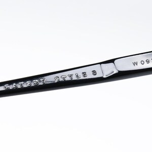 May include: Close-up of a black and silver metal object. The text "CATSEYE STYLE 3" and "W 0936" are visible. The object has a shiny, reflective surface.