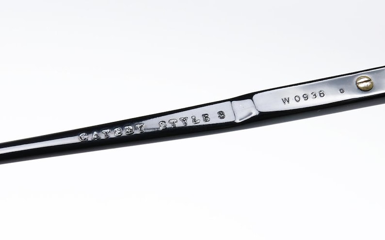 May include: Close-up of a black and silver metal object. The text "CATSEYE STYLE 3" and "W 0936" are visible. The object has a shiny, reflective surface.